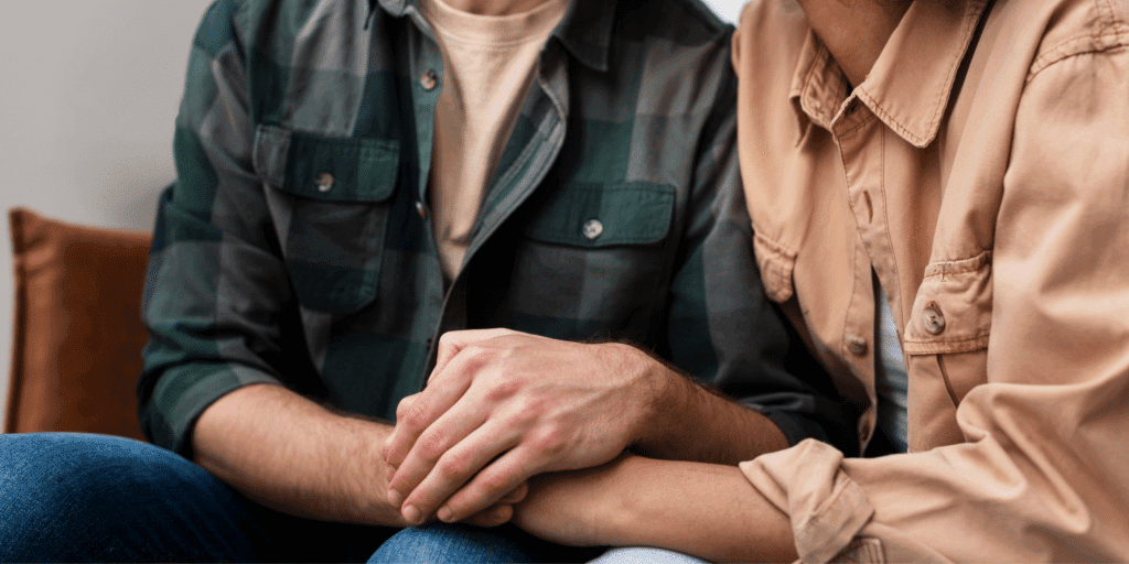 He should trust you. A closeup photograph of a man in a plaid shirt holding the hands of his female partner while sitting on the couch at home.