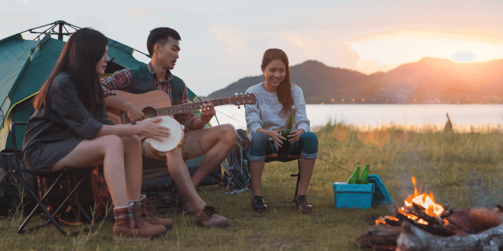 Signs of a Situationship. A man plays guitar with two women sitting beside him in front of a tent at their campsite.