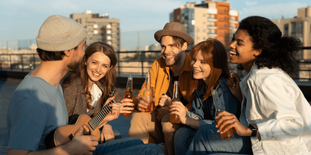 A group of friends sit on a city rooftop playing music and singing together exhibiting signs of a situationship and casual dating.