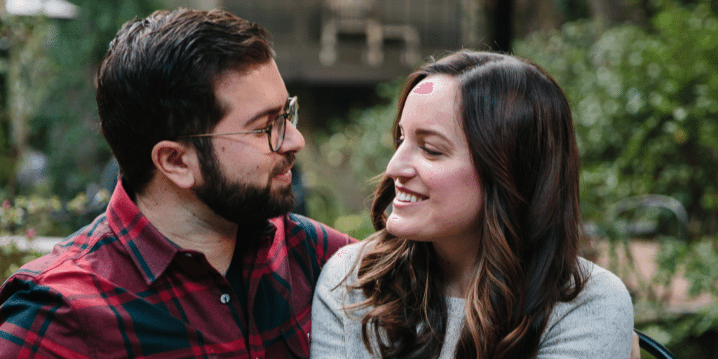 Matchmaking vs online dating. A bearded man in a red flannel shirt and glasses lovingly looks at a brunette woman who smiles back at him.