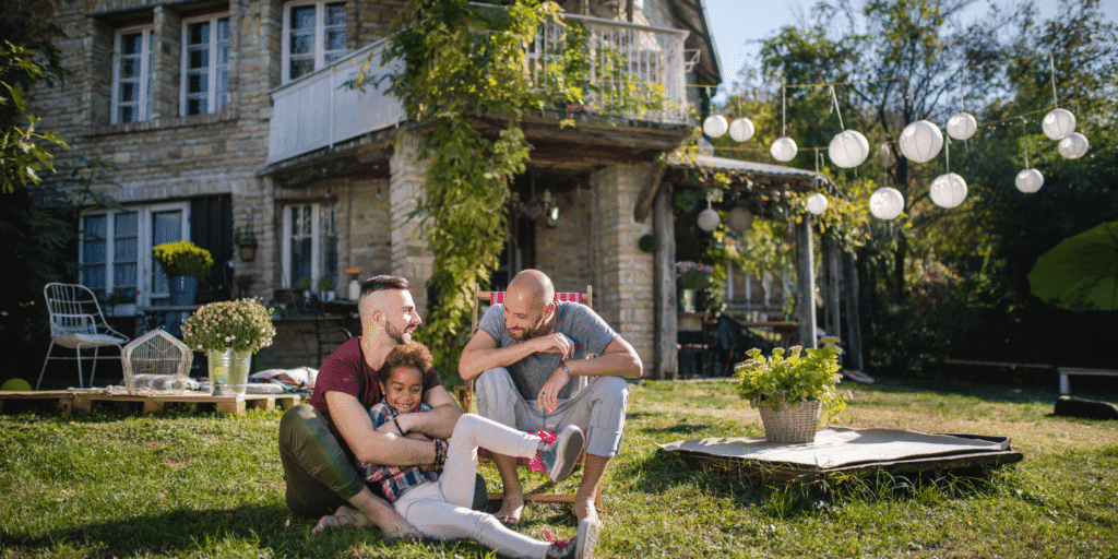 A husband and husband couple play in the backyard with their daughter to illustrate the gay dating tip of accepting each other's identity.