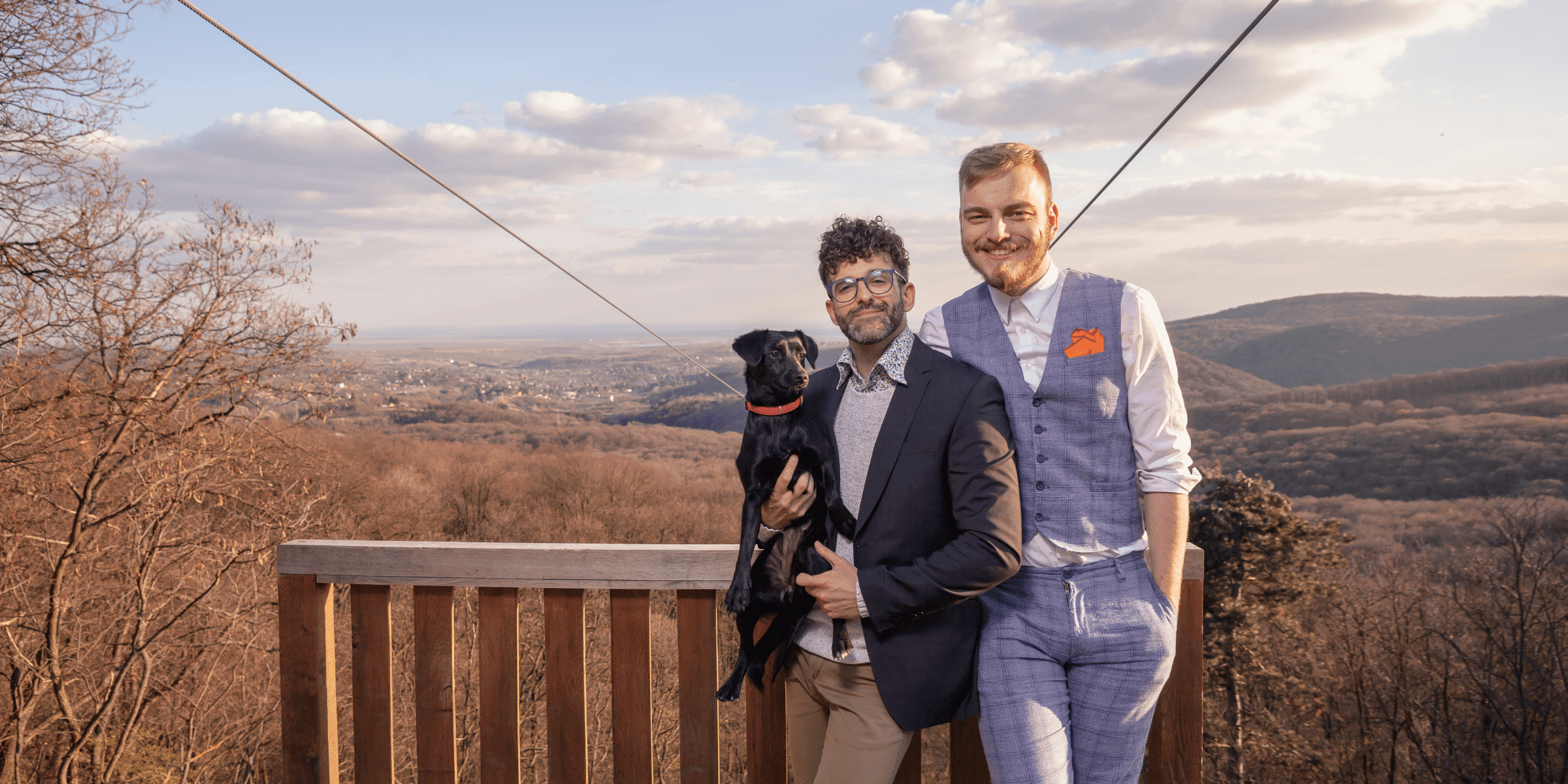 Generational differences are common for gay men who date as shown by this photo of a young gay man in a suit hugging an older gay man with a small black dog in his arms.