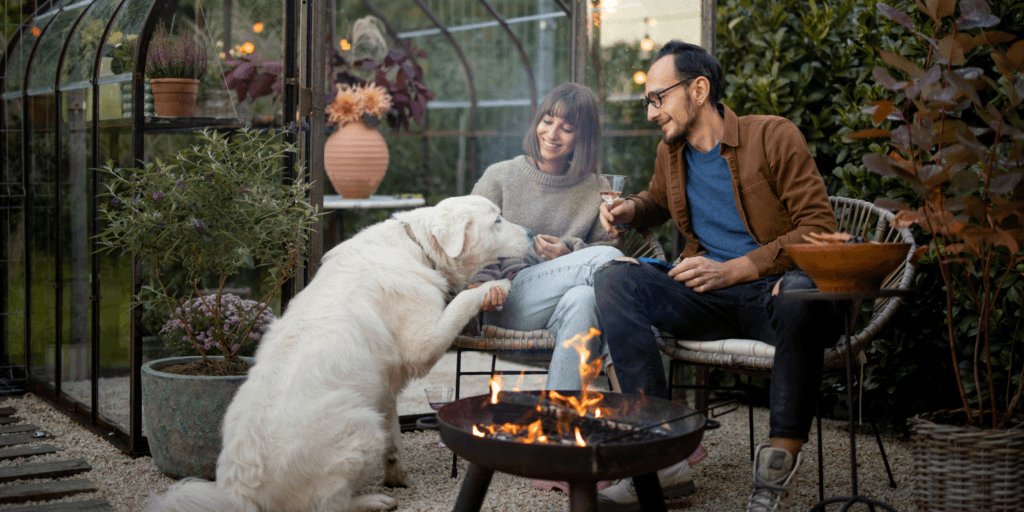 A couple sit in front of a patio campfire with a white dog enjoying a date in New Jersey.