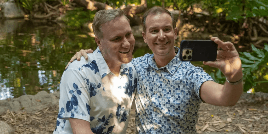 A happy male couple take a selfie in a park after their first matchmaker consultation.