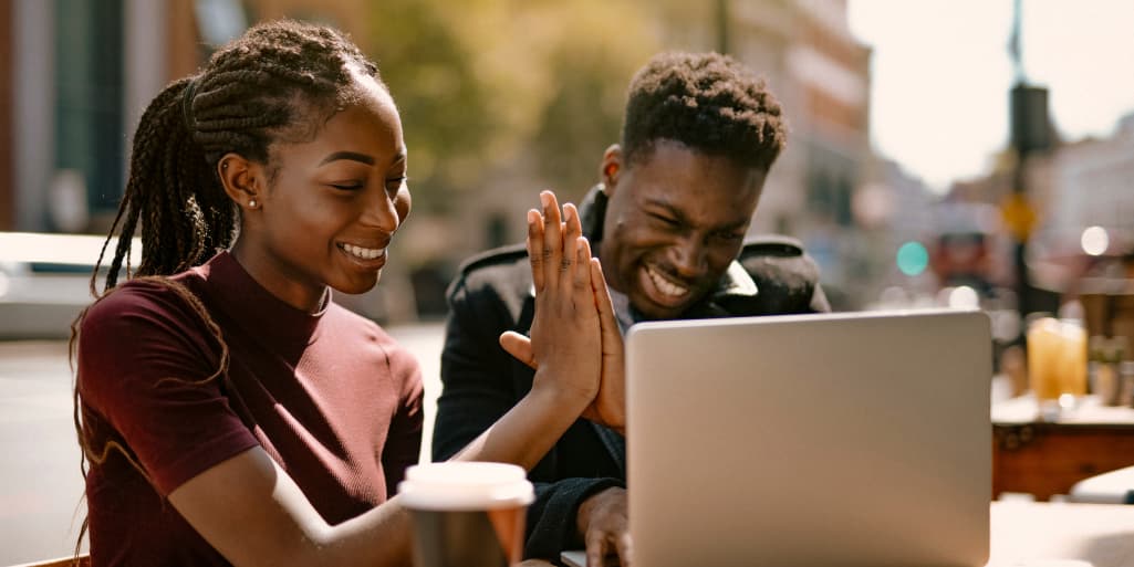 Couple high-five while looking at a laptop at an outdoor café.
