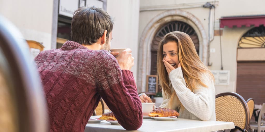A smiling couple shares coffee at an outdoor cafe, capturing the low-pressure vibe of a great first date spot.