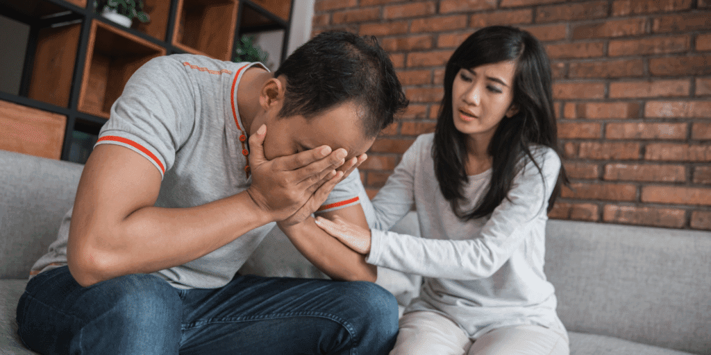 He should be okay with being vulnerable. A man holds his hands to his face and cries while his girlfriend consoles him.
