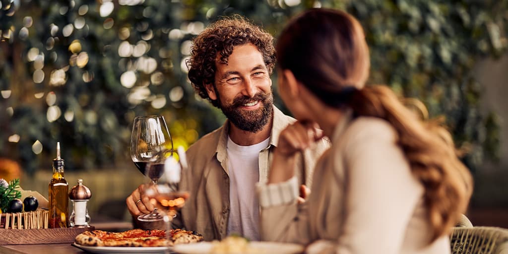 Smiling couple talking over wine and pizza during a dinner date on a restaurant patio