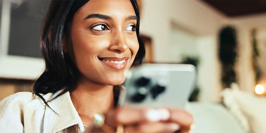 A woman smiles holding her mobile phone as she learns what matchmakers do and what to expect in her first matchmaker consultation.